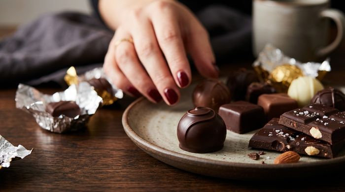 Femeie alegând o pralină dintr-o farfurie cu ciocolată neagră asortată și trufe.